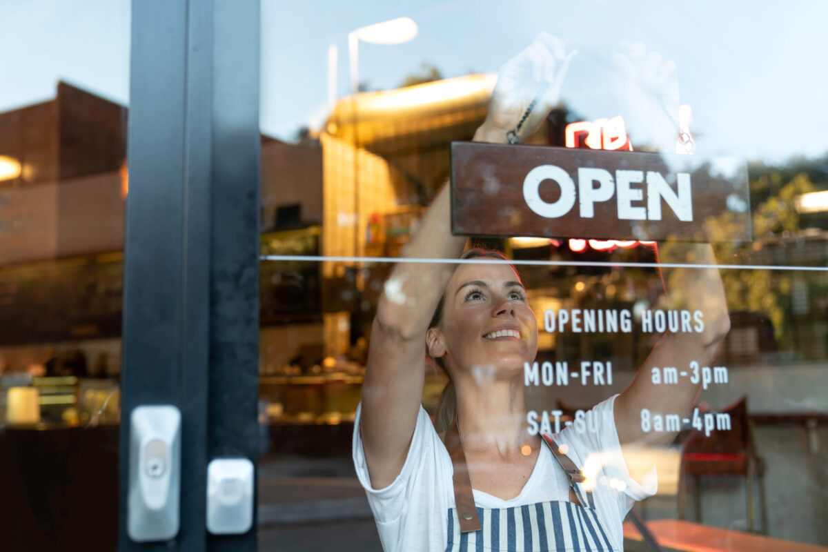 Happy business owner hanging an open sign at a café