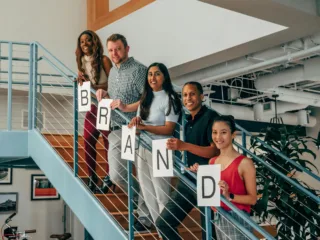 Group of people holding letters that spell out the word "BRAND"