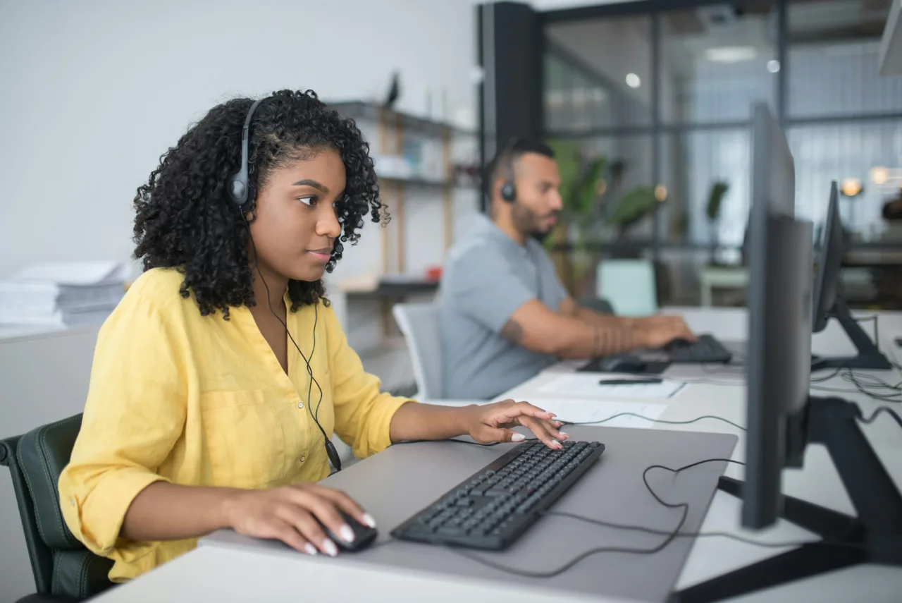 Two people working on their computers with headsets in a modern office setting