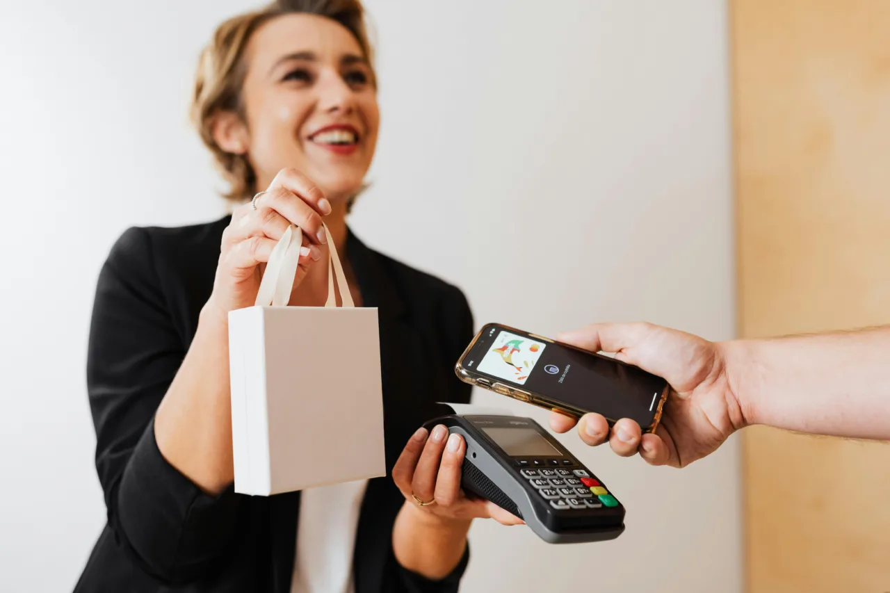 Woman handing a purchase to a customer and presenting a POS for payment