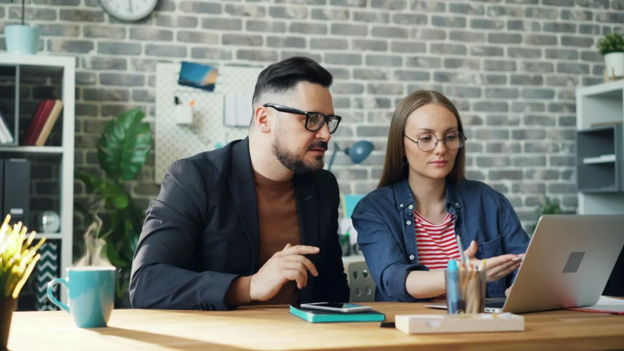 A man and woman collaborating on a project using a laptop at an office desk