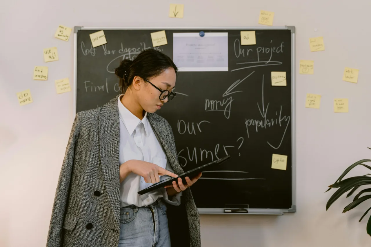 Woman holding a tablet while standing in front of a chalk board